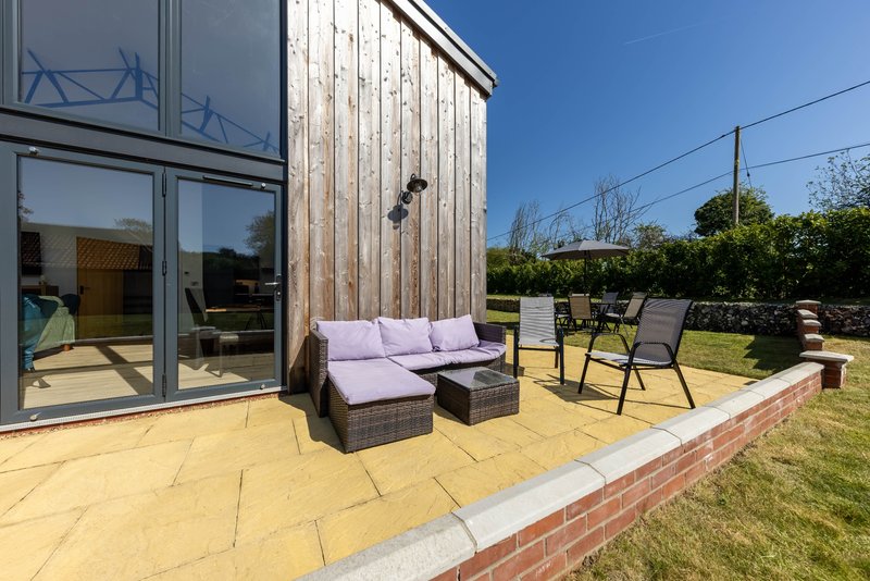 Modern patio area with purple cushioned seating, wooden cladding, and manicured garden