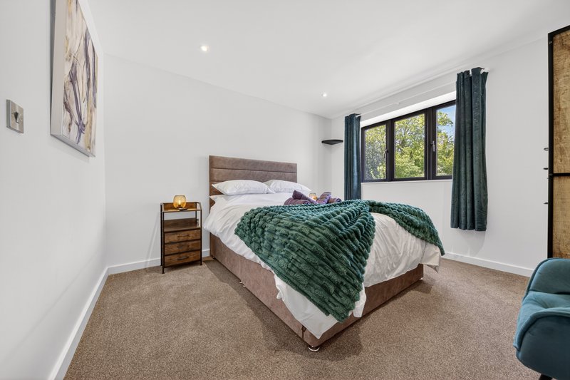 Bright bedroom with double bed, green bedding, wooden headboard, and carpeted floor