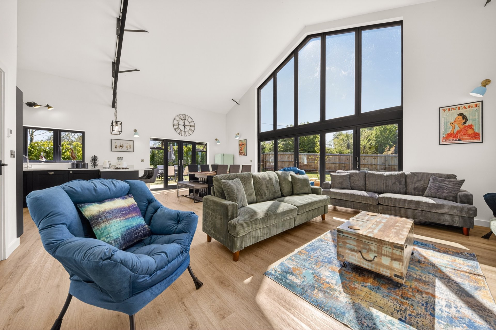 Spacious open-plan living room with blue armchair, grey sofas, wooden floor and large windows