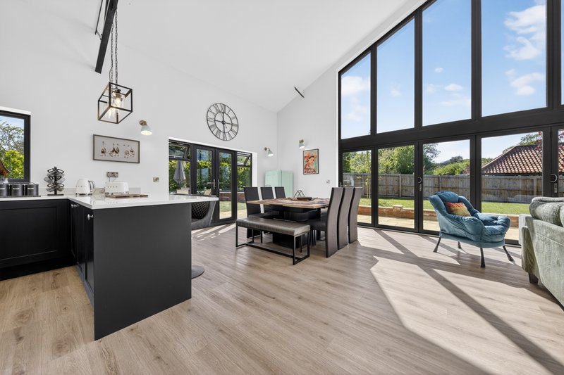 Open-plan kitchen and dining area with black island, wooden flooring, large windows and garden views