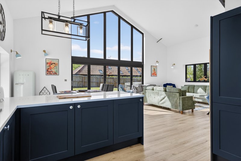 Modern open-plan living space with black kitchen island, large windows, and light wood flooring