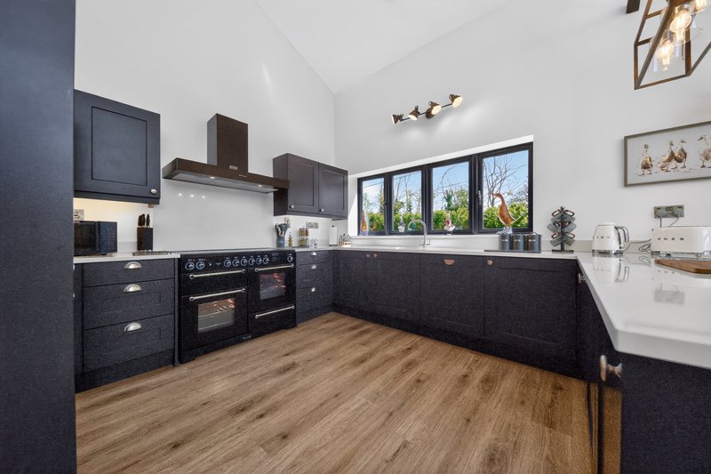 Modern kitchen with dark cabinetry, black range cooker, wooden flooring and large windows