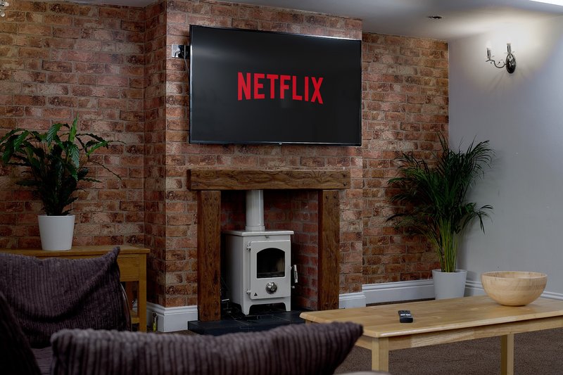 A comfortable and inviting living room with a feature brick fireplace, wood-burning stove and wall-mounted TV with Netflix, creating a cosy space for guests to relax and unwind.