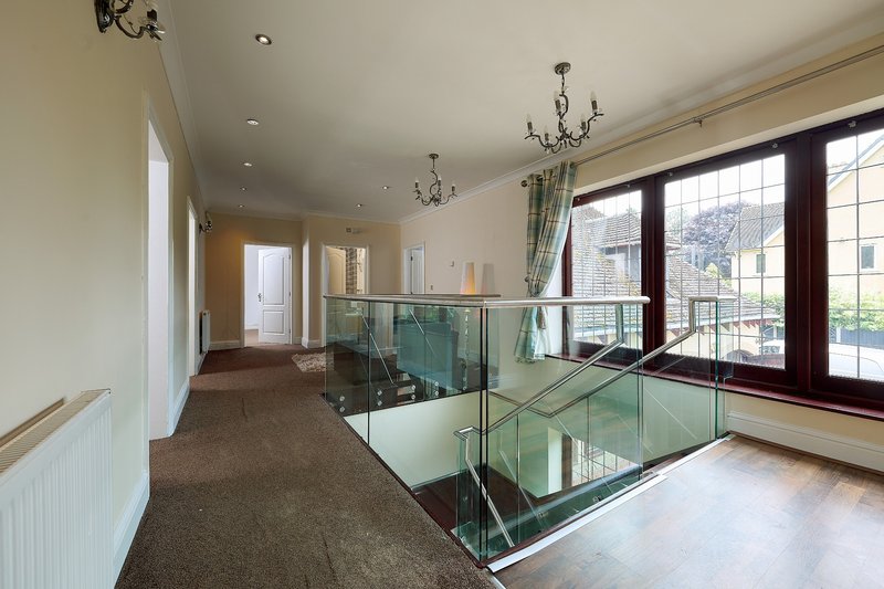 A spacious first-floor landing with a bright, open feel, featuring a stylish glass balustrade, large windows and plenty of natural light.