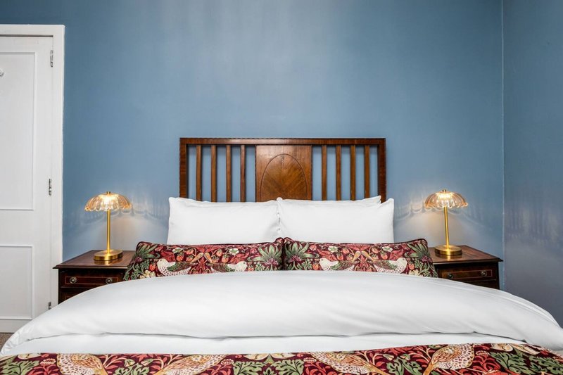 Bedroom with wooden bed frame, white pillows, patterned bedding, blue walls, bedside lamps