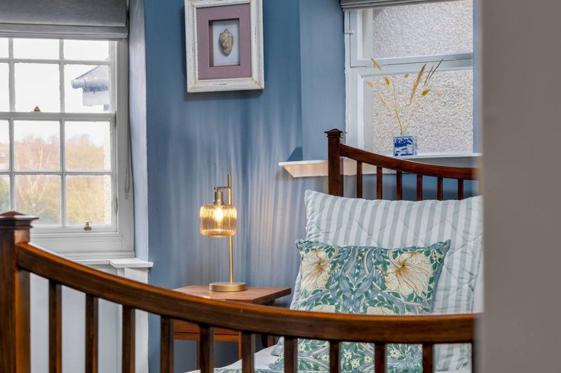 Nursery corner with wooden crib, blue striped walls, window, lamp and decorative cushions