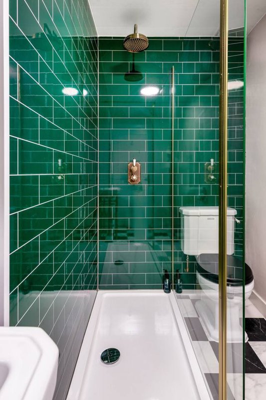 Modern bathroom with emerald green subway tile shower enclosure, brass fixtures and white basin