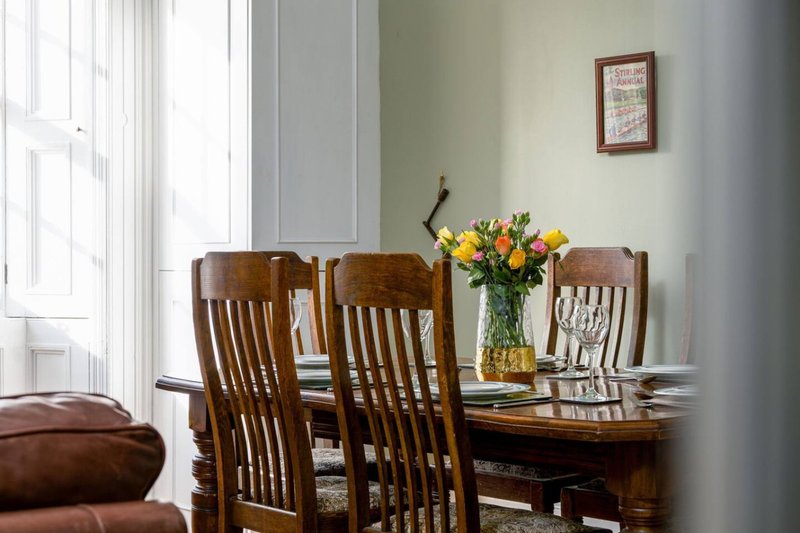 Dining room with wooden table, chairs, fresh flowers in vase, and bright natural light from windows