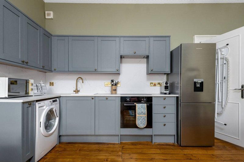 Modern kitchen with blue cabinetry, stainless steel appliances, white countertop and wooden floor