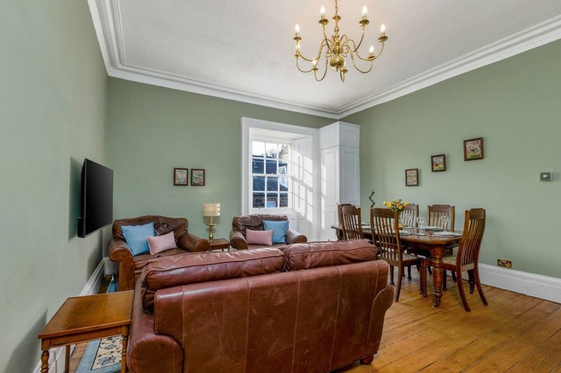 Spacious living room with green walls, leather sofa, dining table and chairs, wooden floor
