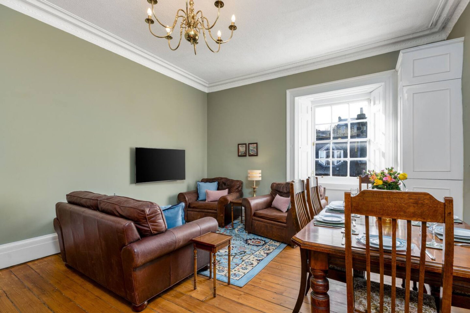 Spacious living room with leather sofa, wooden dining table, windows and chandelier