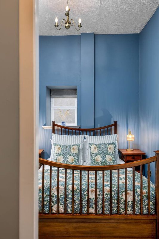Nursery with wooden crib, blue accent wall, brass chandelier and window with natural light