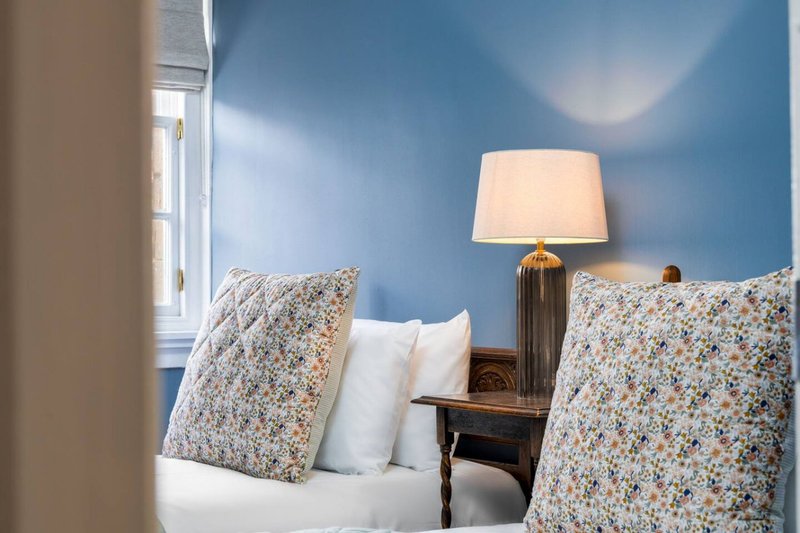 Bedroom with blue walls, double bed, patterned cushions, bedside lamp and window