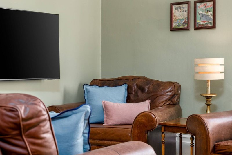 Living room with brown leather sofa, blue and pink cushions, wall-mounted TV, and table lamp