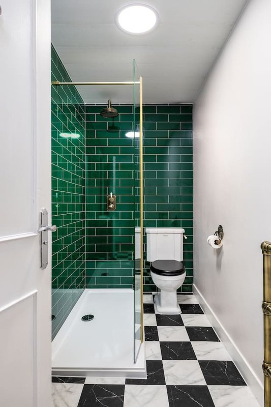 Modern bathroom with green subway tile shower, black and white checkered floor, white toilet and towel rail