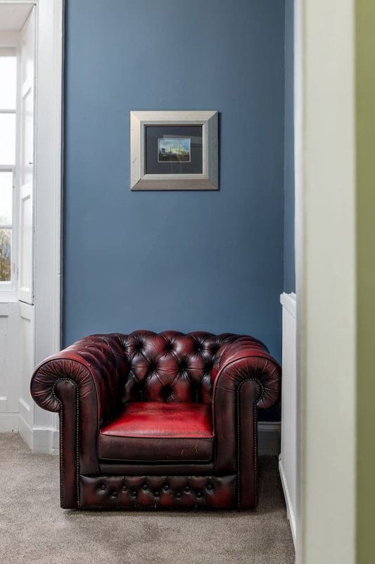 Blue-walled hallway with burgundy leather Chesterfield armchair and framed artwork