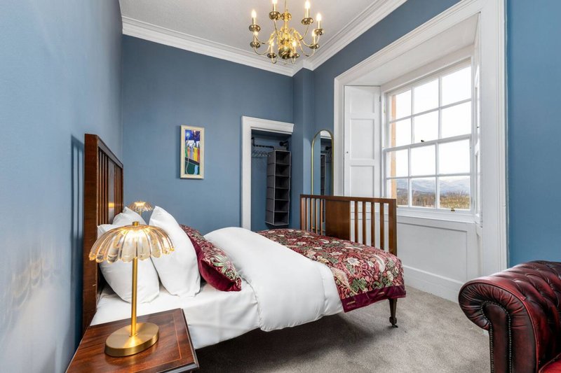 Bedroom with double bed, blue walls, wooden frame, gold chandelier and large window