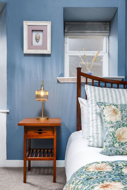 Bedroom with blue walls, wooden bedside table, brass lamp, and floral patterned bedding