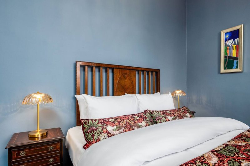 Modern bedroom with double bed, wooden headboard, white pillows, patterned throw, brass lamp and framed artwork