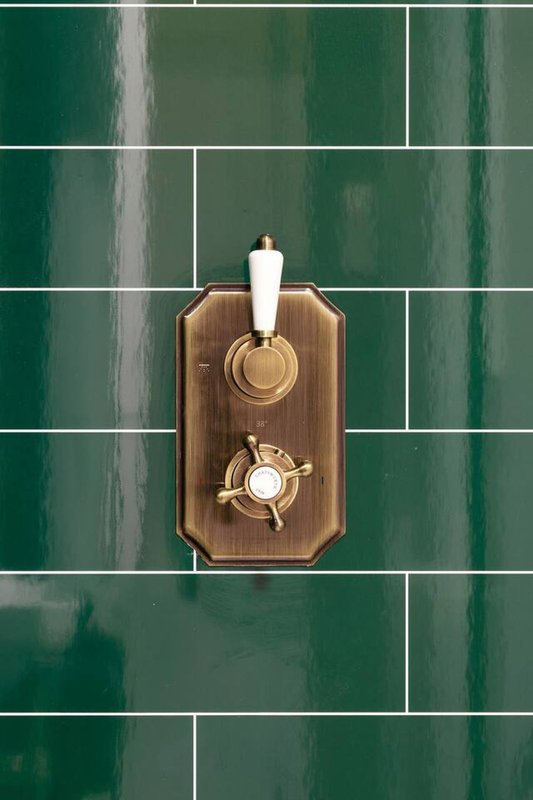 Green tile bathroom wall with decorative wooden board and brass fixtures