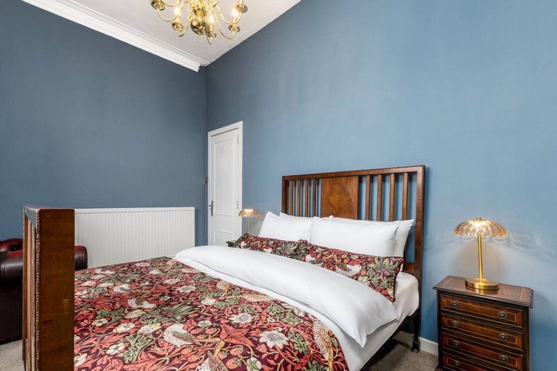 Bedroom with double bed, blue walls, wooden furniture, brass chandelier and bedside lamp