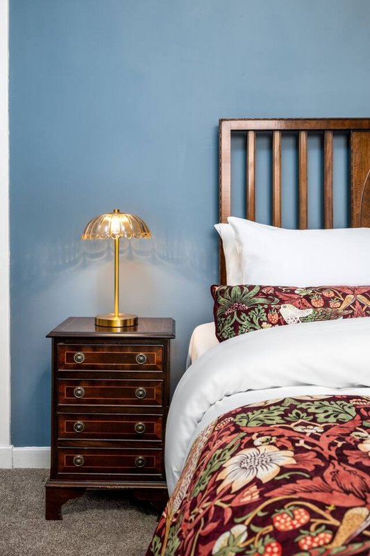 Bedroom with blue accent wall, wooden bed frame, bedside table with brass lamp and white pillows