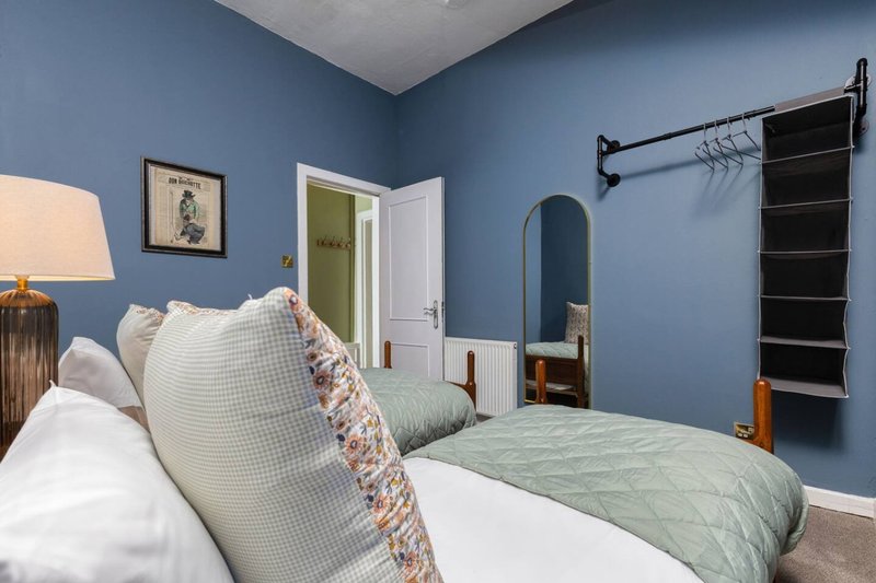 Blue bedroom with double bed, white pillows, green bedding and wooden furniture