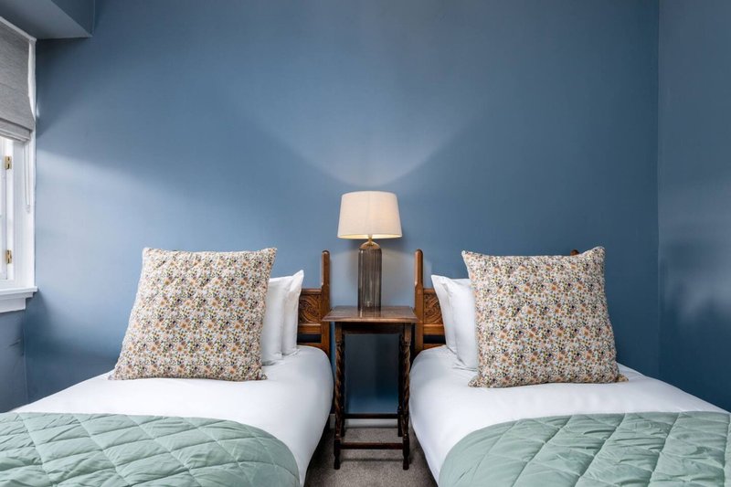 Twin bedroom with blue walls, white pillows, patterned cushions and bedside lamp