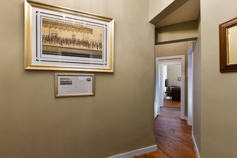 Hallway with framed artwork on walls, wooden flooring and doorway leading to other rooms