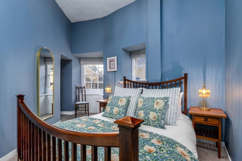 Bedroom with blue walls, wooden bed frame, patterned bedding, and bedside tables with lamps