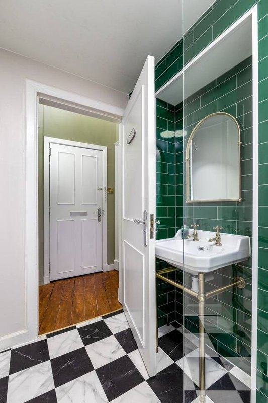 Modern bathroom with green tile wall, round mirror, pedestal sink and checkered floor