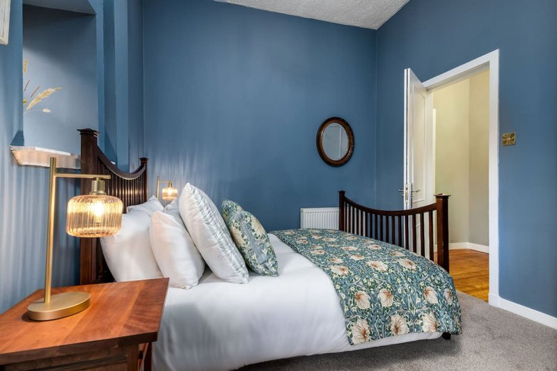 Modern bedroom with double bed, blue walls, wooden bedside table and brass lamp