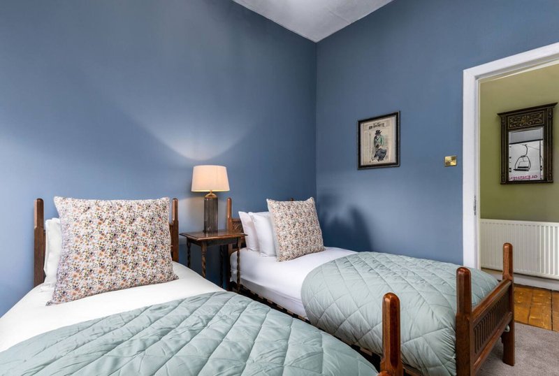 Bright bedroom with two single beds, blue walls, wooden bedframe and small side table with lamp