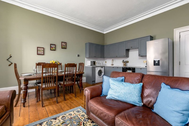 Open-plan living and dining area with leather sofa, dining table, kitchenette and sage green walls