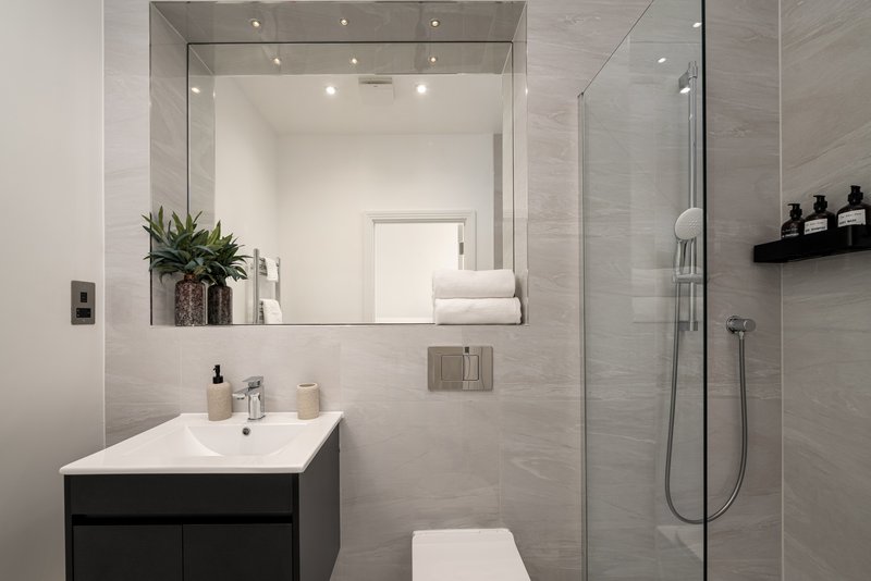 Modern bathroom with white sink, black vanity, large mirror, shower enclosure and grey tile walls
