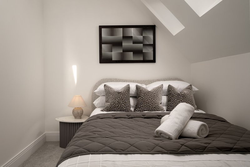 Modern bedroom with double bed, gray bedding, decorative pillows, wall-mounted shelving unit and table lamp