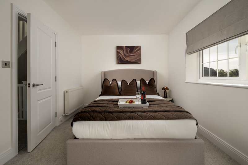 Compact bedroom with double bed, brown bedding, decorative pillows and small window