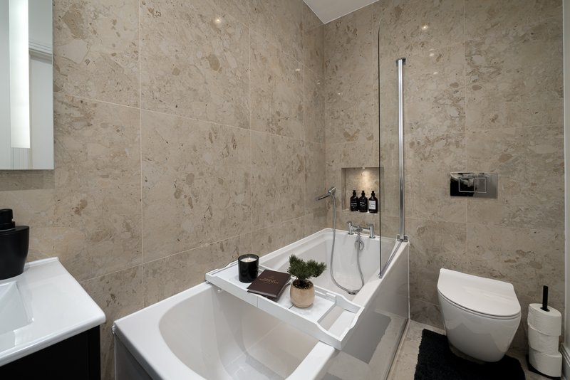 Modern bathroom with bathtub, walk-in shower, toilet, and neutral stone tile walls