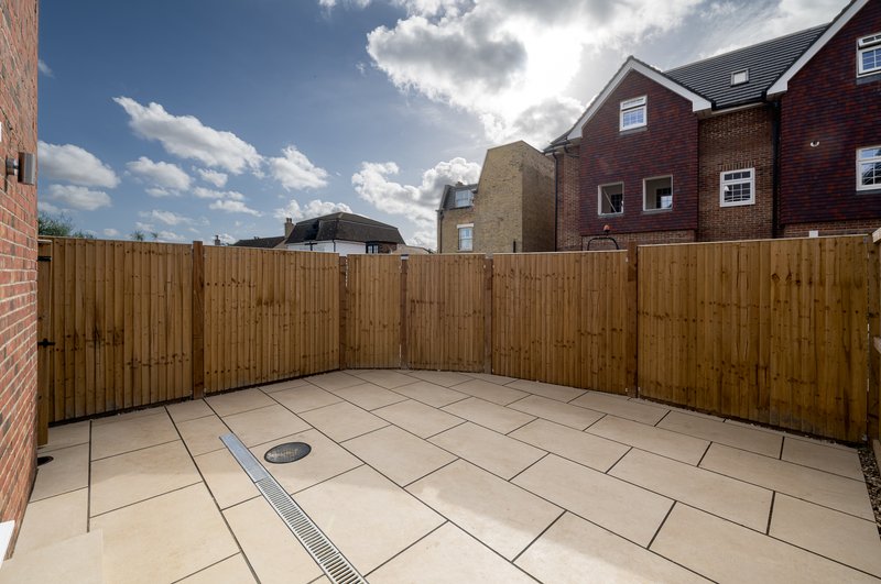 Paved outdoor courtyard with wooden fence, surrounded by brick residential buildings