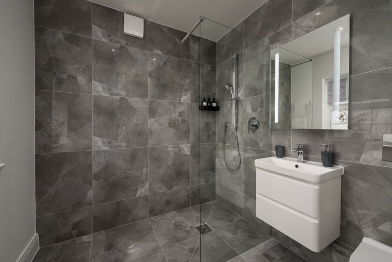 Modern bathroom with grey tile walls, walk-in shower, white vanity and mirror