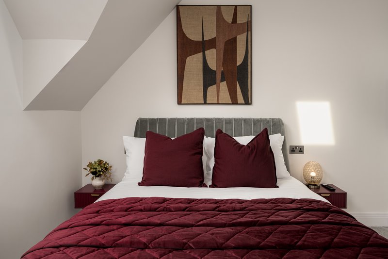 Modern attic bedroom with burgundy bedding, grey headboard, wall art and bedside lamps
