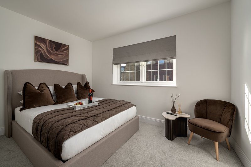 Modern bedroom with grey upholstered bed, brown bedding, armchair and large window