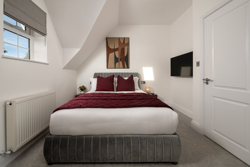 Attic bedroom with double bed, burgundy bedding, small TV mounted on wall