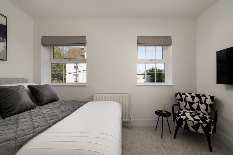 Modern bedroom with double bed, windows, wall-mounted TV, and geometric patterned chair