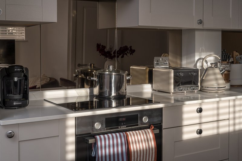 Modern white kitchen with stainless steel appliances, countertop cookware, and natural lighting