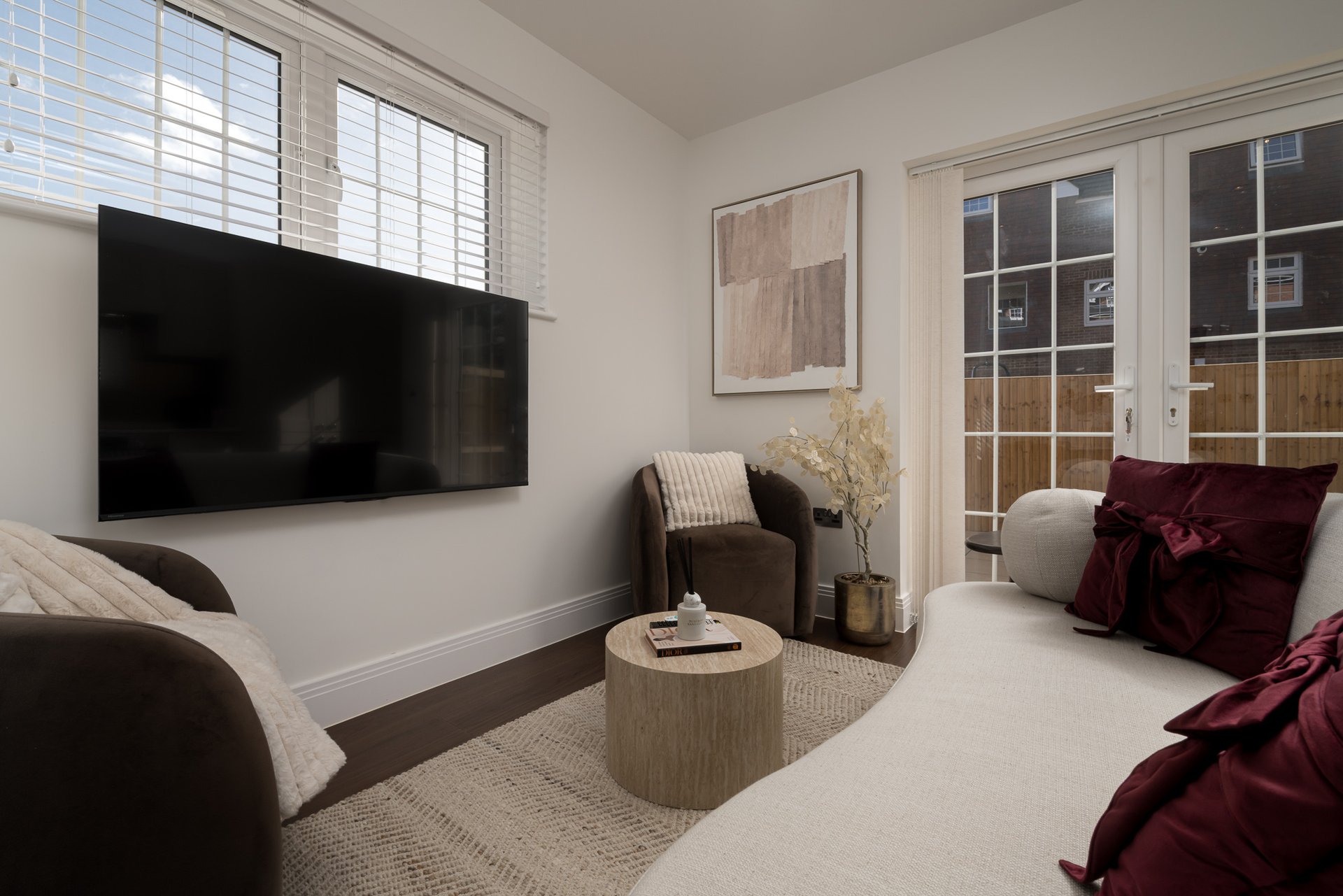 Modern living room with wall-mounted TV, cream carpet, dark sofa and burgundy velvet cushions