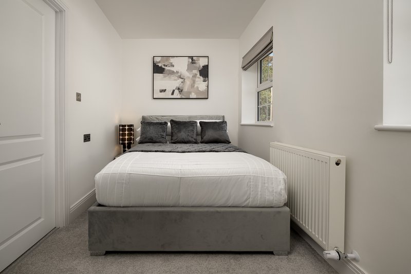 Compact bedroom with double bed, grey upholstered frame, white bedding and dark pillows