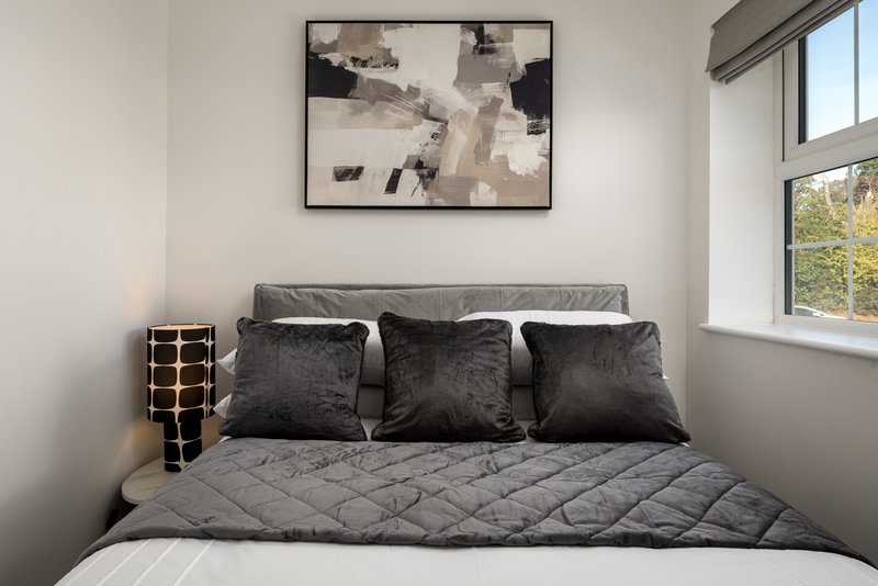 Modern bedroom with grey quilted bedding, dark cushions, framed abstract artwork and window