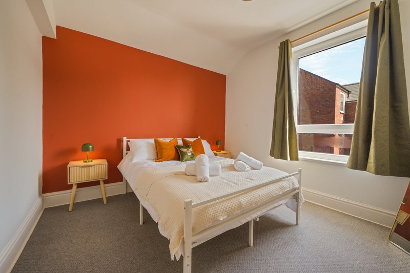 Bright bedroom with orange accent wall, white bed, wooden nightstand and large window