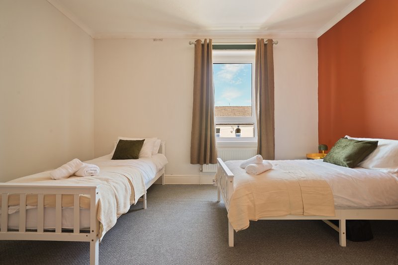 Bright bedroom with two single beds, orange accent wall, and window with countryside view